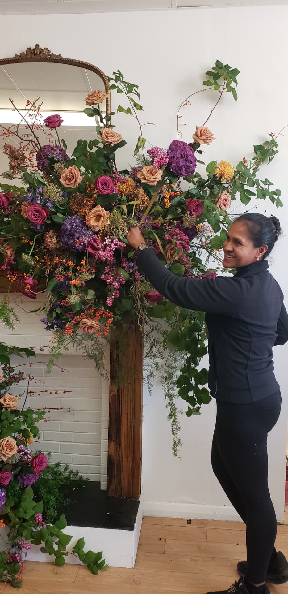 Kara of Dolce Flowers arranging a lush mantel installation of roses and greenery in her Greenville, SC studio