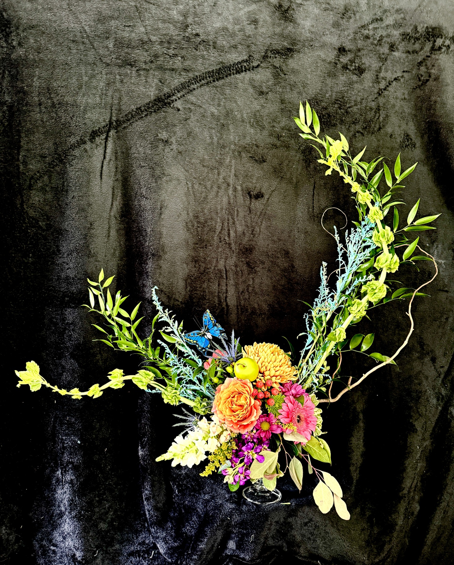 Colorful crescent-shaped arrangement with garden roses and butterfly accent, photographed on a dark backdrop by Dolce Flowers in Greenville, SC
