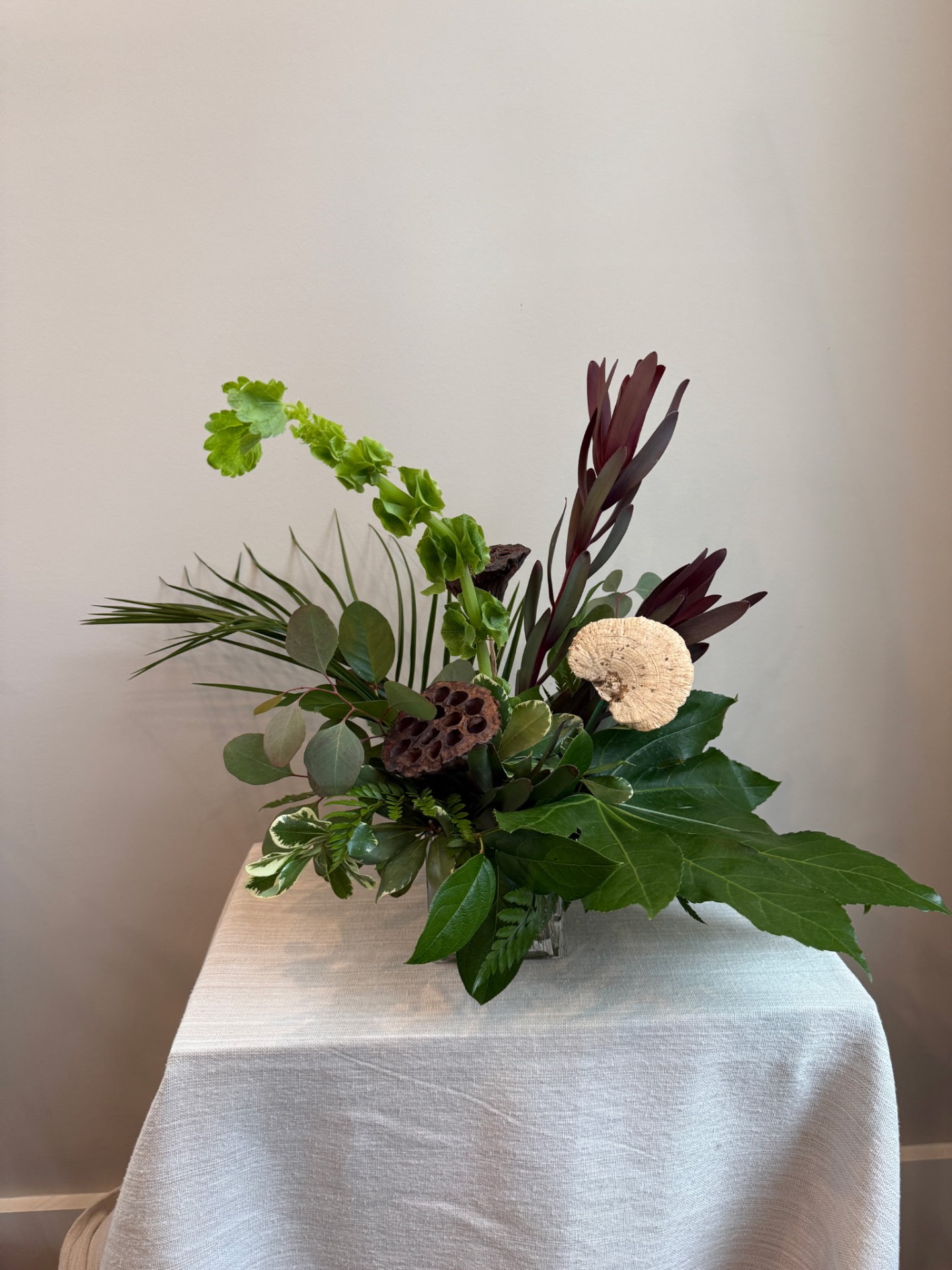 Green and burgundy foliage arrangement with lotus pods and leucadendron by Dolce Flowers in Greenville, SC