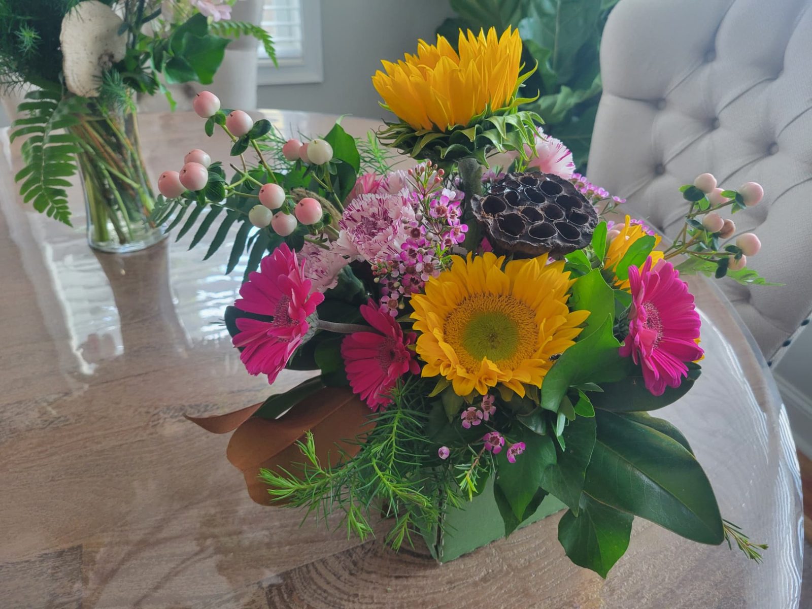 Side view of a sunflower and pink gerbera daisy closing gift arrangement on a dining table, by Dolce Flowers in Greenville, SC